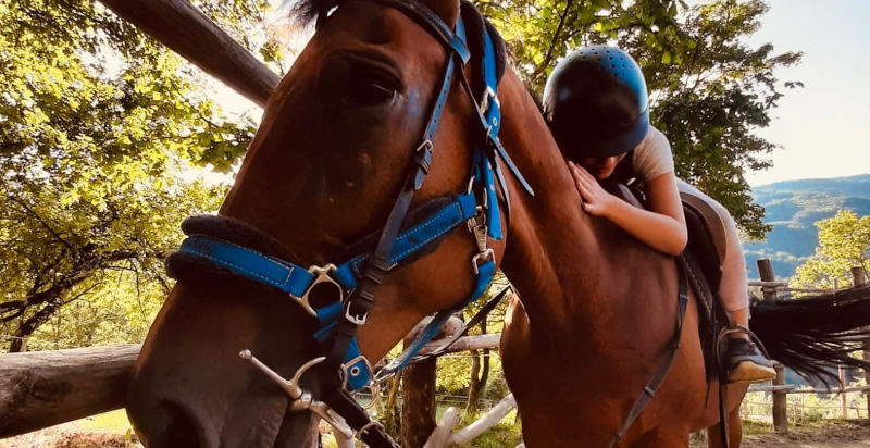 Bambino con casco abbraccia un cavallo durante una passeggiata nelle campagne pistoiesi