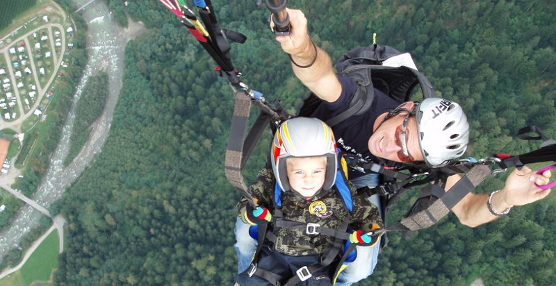 Bambino vola con pilota in un volo in parapendio in montagna