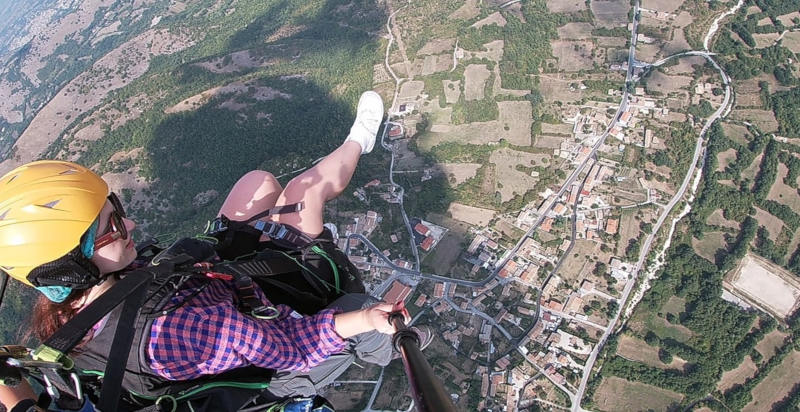Pilota di parapendio con passeggero in volo sopra il paesaggio abruzzese